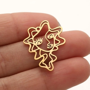 Golden abstract face pendant in stainless steel held between fingers on white background
