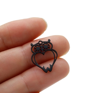Black stainless steel hollow owl pendant with heart cutout held by fingers for scale