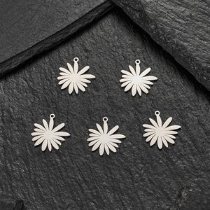 Gros plan de cinq pendentifs marguerite argentés sur roche pour création de bijoux