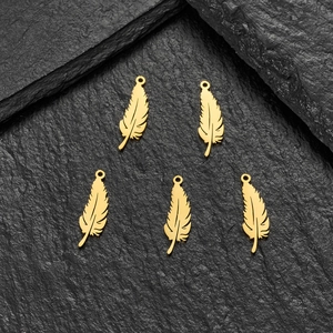 Detail of five mini matte gold feather charms for DIY jewelry making on stone background