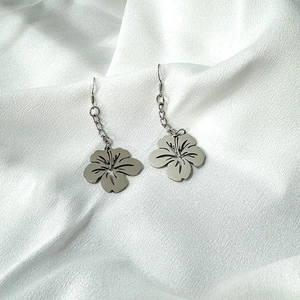 Detailed close-up of silver stainless steel five-petal flower drop earrings on white silk