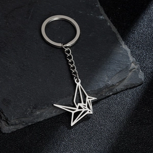 Modern hollow origami crane keychain in polished stainless steel on a dark stone surface