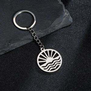 Close-up of silver hollow keychain featuring sunburst and ocean waves on rock background