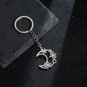 Detailed close-up of a silver crescent moon keychain with delicate hollow flower patterns