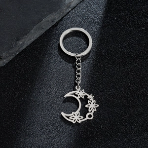 Silver stainless steel crescent moon keychain with hollow flower charms on black surface