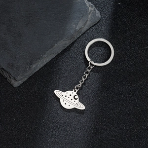 Silver stainless steel Saturn planet keychain with celestial cutouts on black stone surface