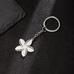 Polished stainless steel flower pendant keychain on a minimalist black textured surface