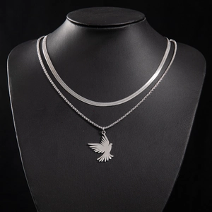 Close-up of layered stainless steel snake chain and box chain with flying bird pendant