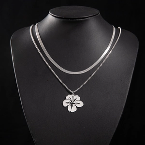 Detail of silver double-layered necklace featuring a floral pendant on a dark neck bust