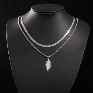 Detail of silver layered necklace with flat snake chain and textured feather pendant
