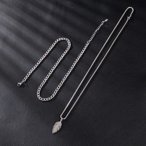 Close-up of silver feather pendant with chunky cuban chain on black leather surface