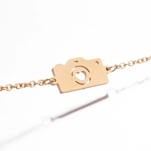 Gros plan sur un bracelet doré avec pendentif appareil photo et détail coeur évidé