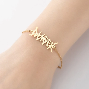 Detailed view of a gold gothic letter charm on a minimalist chain bracelet on wrist