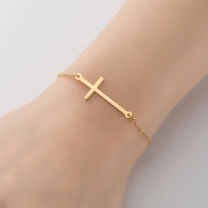 Gros plan d'un bracelet minimaliste en or avec pendentif croix porté au poignet