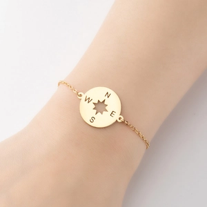 Detailed close-up of a gold compass pendant bracelet with N S E W directional engravings