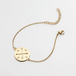 Detail of gold compass bracelet with N E S W engraving on white background