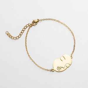Détail d'un bracelet doré ajustable doté d'un pendentif abstrait au visage irrégulier