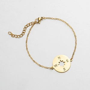 Detail of gold stainless steel compass bracelet with engraved cardinal directions N E S W