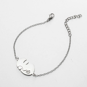Détail d'un bracelet argenté avec pendentif visage abstrait et chaîne de réglage fermoir