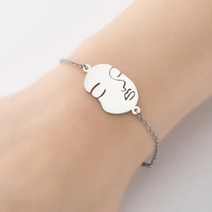 Détail d'un bracelet minimaliste argenté avec pendentif au design de visage abstrait