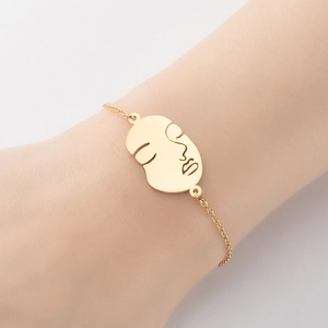 Vue détaillée d'un pendentif visage irrégulier sur un fin bracelet en chaîne dorée