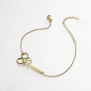 Detail of golden stainless steel bracelet featuring a vintage-style scissors charm and clasp