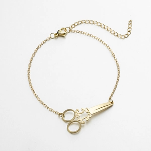 Detail view of gold scissor charm bracelet with ornate handle and lobster clasp chain