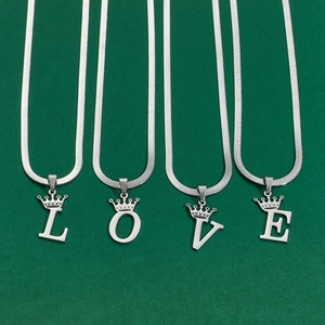 Detailed macro view of four silver crown initial necklaces spelling LOVE on green surface