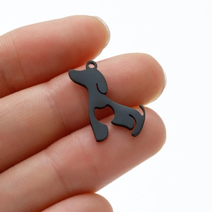 Black dog pendant in stainless steel held by hand for scale on a white background