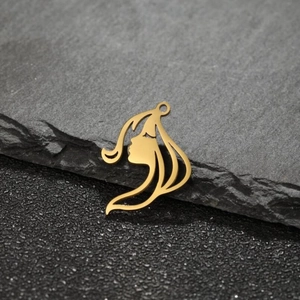 Macro shot of gold-plated cutout girl face pendant on dark natural stone surface