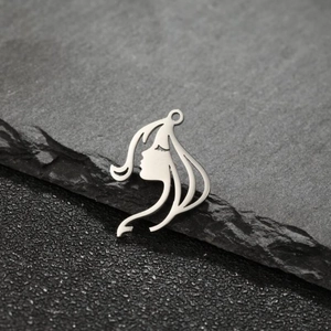 Detail of silver fairy face pendant with long hair profile on dark stone surface