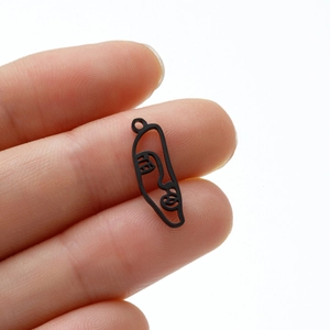 Macro view of a small black stainless steel abstract face pendant on a fingertip