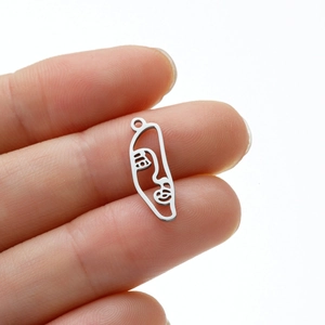 Detailed view of silver abstract face pendant held by fingers to show actual product size