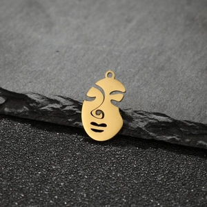 Macro shot of gold abstract face pendant on textured stone background for DIY jewelry