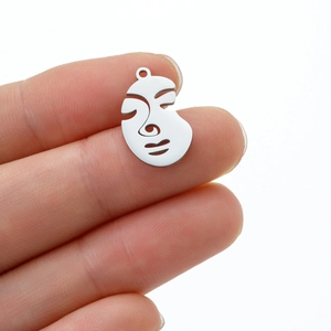 Close-up of silver minimalist abstract face pendant held by fingers to show scale