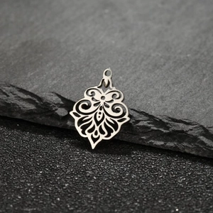 Close-up of stainless steel Tree of Life hollow charm on a natural grey rock background