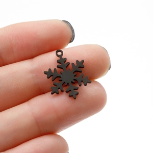 Macro shot of a matte black snowflake pendant held by fingers to show mini size
