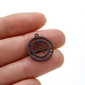Gros plan d'un pendentif en acier inoxydable noir mat avec des symboles occultes ajourés