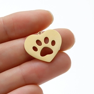 Détail macro d'un pendentif cœur en acier doré avec motif d'empreinte de patte ajourée