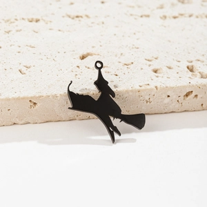Detail view of a matte black witch silhouette pendant on a textured stone surface