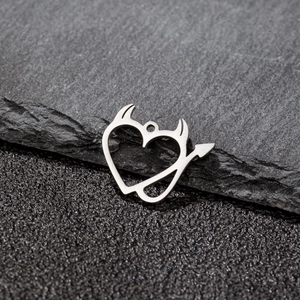 Macro shot of silver devil heart pendant with horns and tail on black stone surface