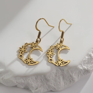 Goldene Edelstahl-Ohrringe mit Halbmond- und Blumenausschnitt auf einer Steinfläche