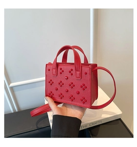 Détail du sac rouge en cuir grainé avec rivets floraux 3D et double poignée