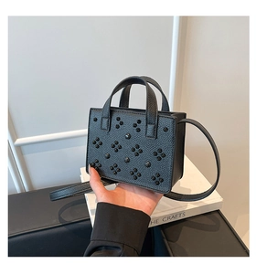Détail du mini sac noir en cuir grainé avec motif floral en rivets sur un livre