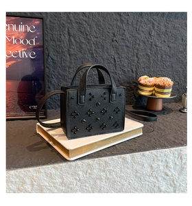 Détail du sac bandoulière en cuir noir avec rivets décoratifs sur des livres blancs