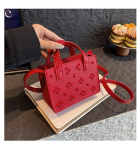 Gros plan du sac bandoulière rouge avec rivets floraux 3D sur un socle blanc