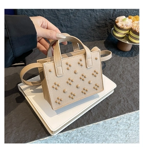 Détail du sac beige en cuir litchi avec motif floral clouté et doubles poignées