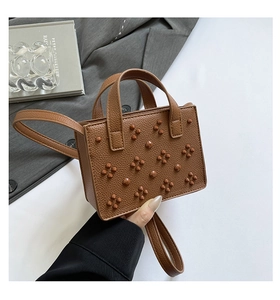Gros plan d'un sac à main marron avec texture litchi et détails de rivets floraux