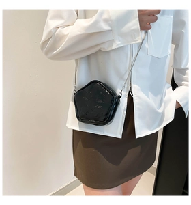 Close-up of black star shaped crossbody bag with embossed patterns and metal chain on model