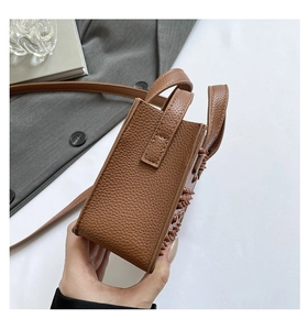 Détail du sac en cuir litchi marron foncé avec bords cloutés et structure carrée